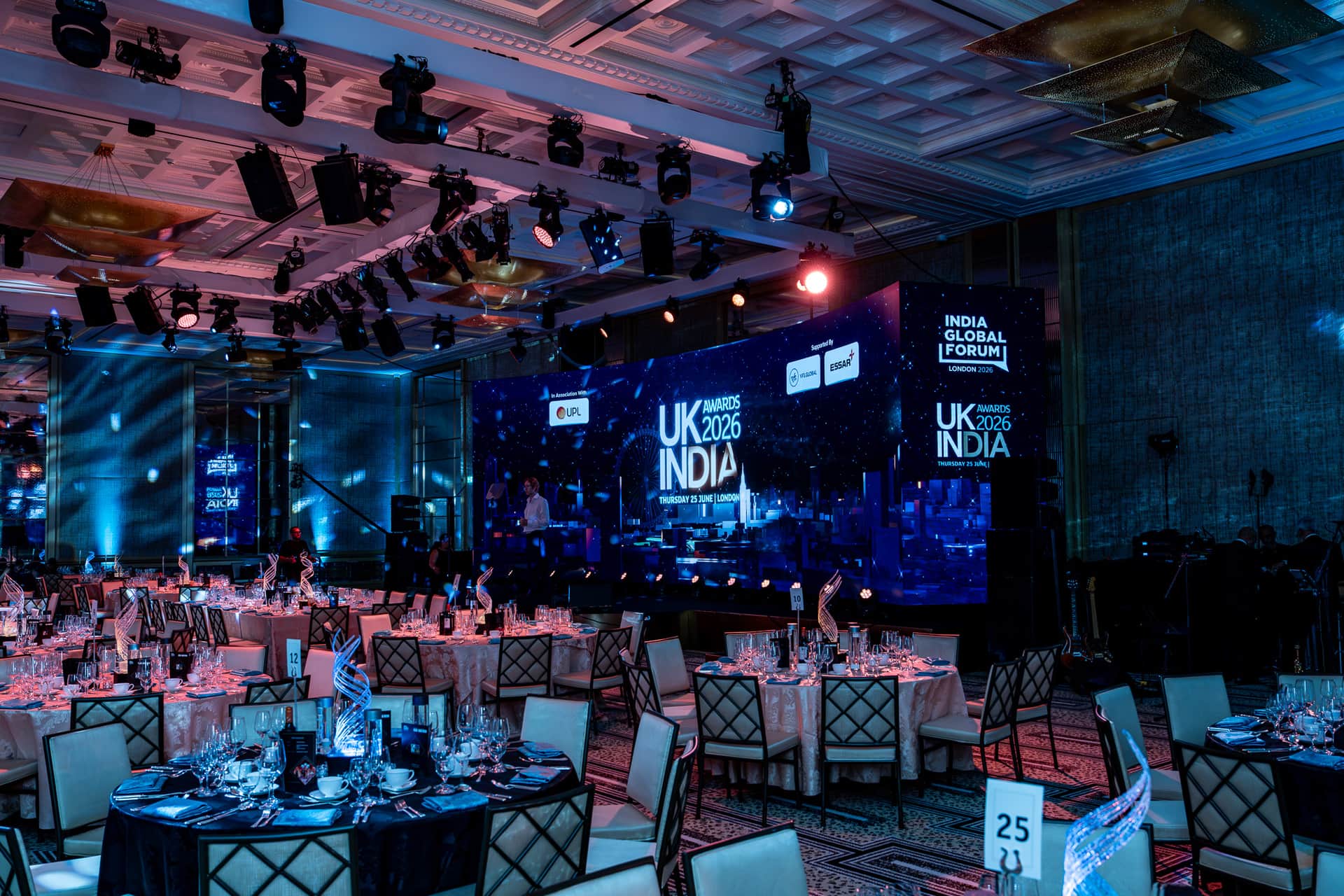 A curved LED stage with an overhead moving-head rig and clear sightlines across the ballroom at the UK-India Awards, staged by Kudos AV